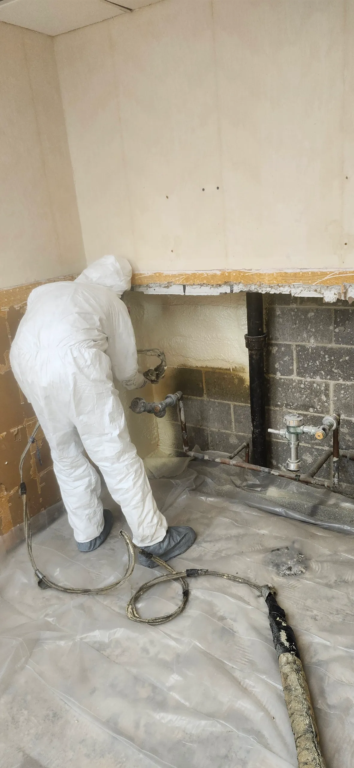 Worker spraying basement block wall around plumbing penetration
